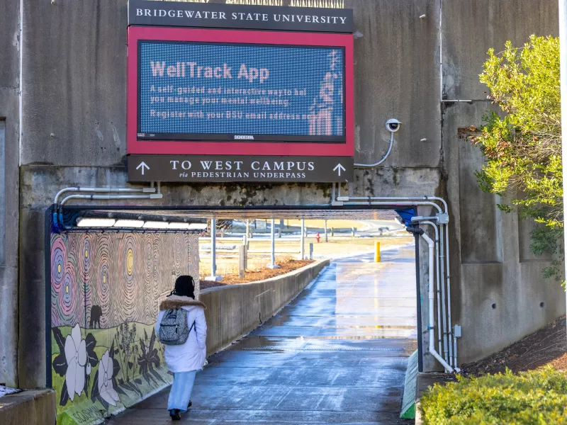 Student walking through a tunnel with University sign and Axis camera visible