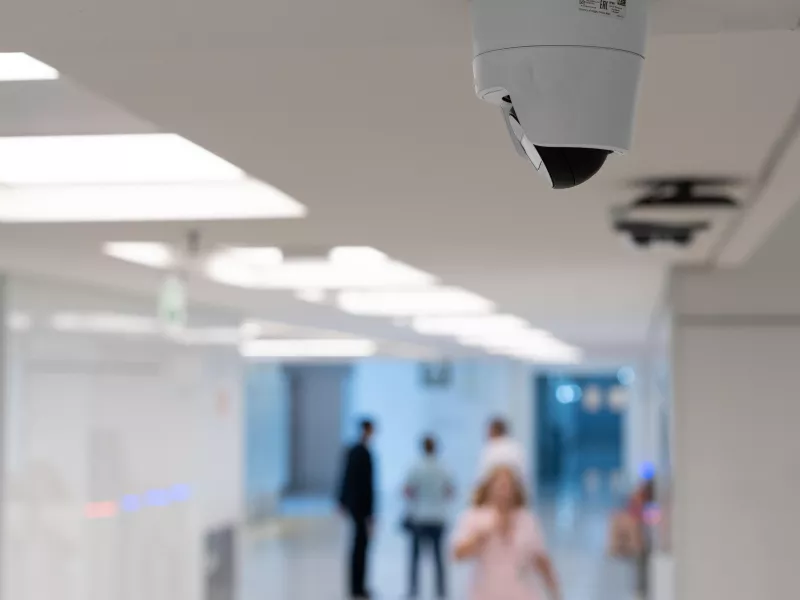 Camera on ceiling of hospital with personnel walking hallway