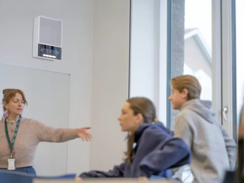 AXIS C1710 installed in a classroom. The display text is Attention and the teacher and studnets are prepring to leave the classroom