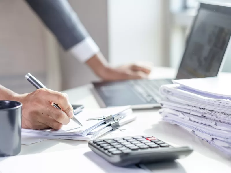 Close up of a business man working on a laptop and writing notes. 