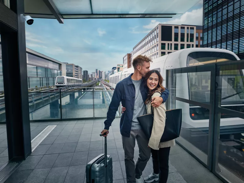 Man and a woman hugging by the train station. An Axis camera is hung to the side of a wall surveilling the area.