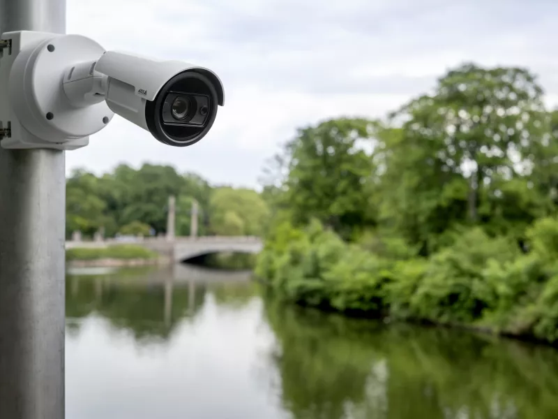 AXIS P1487-LE Bullet Camera mounted on a pole infront of a pond, surrounded by trees