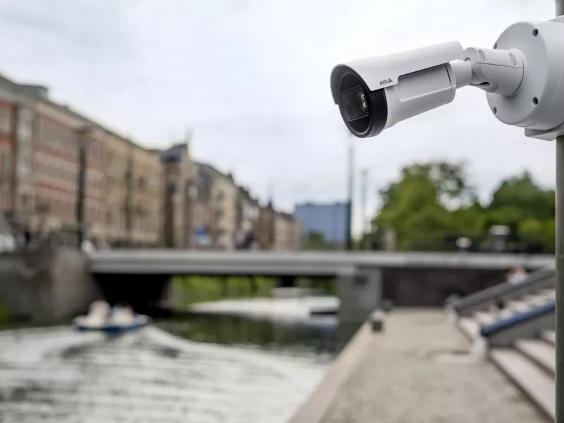 Bullet camera overlooking river in city with blurred buildings in the background