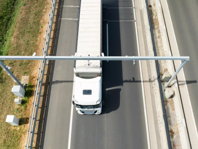 White truck driving through tolling portal on highway.