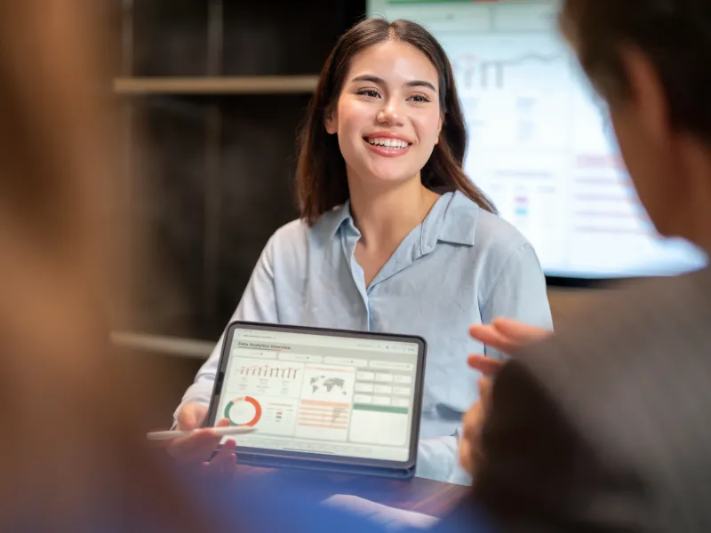 Woman smiling, holding a tablet with graphs and discussing it with coworkers.