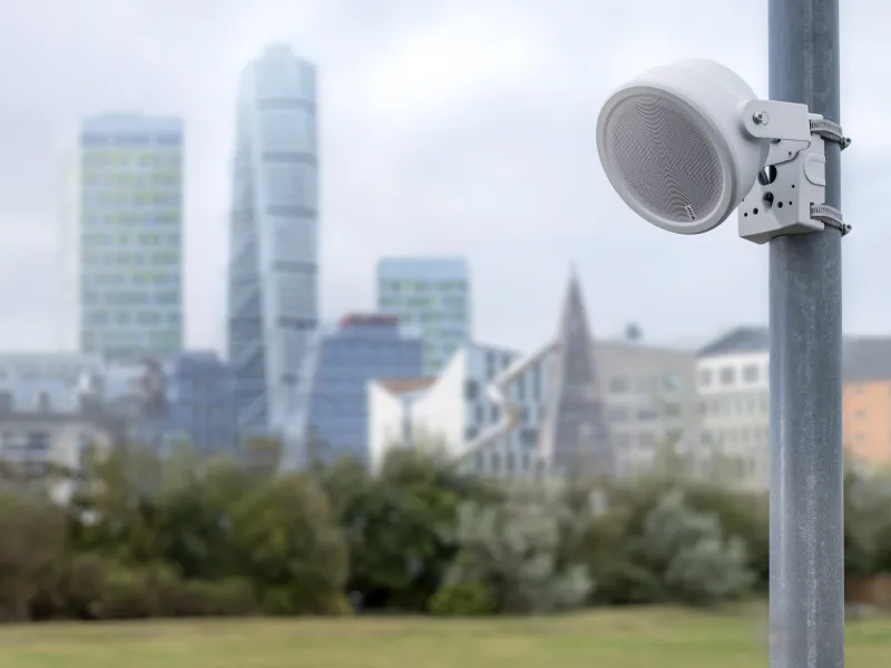 Outdoor network speaker mounted in the foreground with a city skyline and urban buildings in the background
