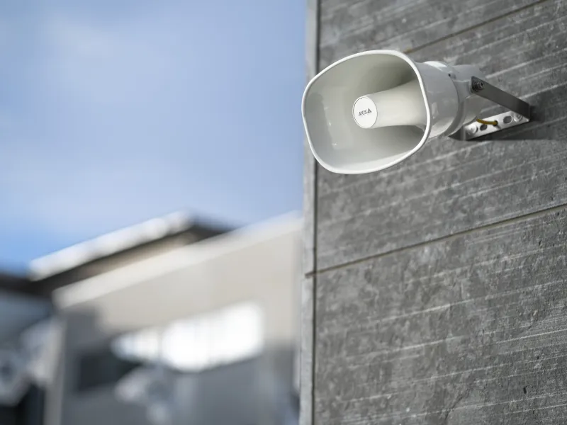 A grey wall of a large building with an Axis horn speaker.