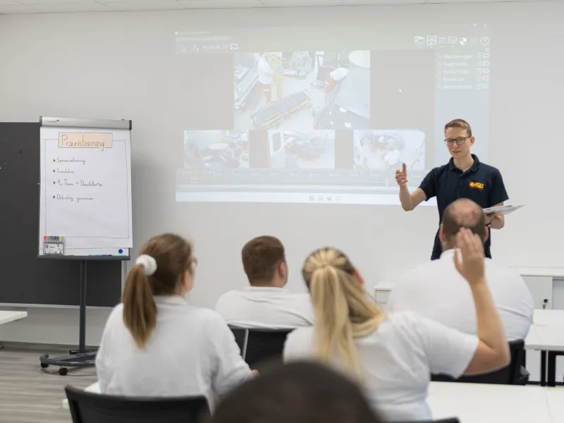 Instructor leading a medical training debriefing in a classroom setting.