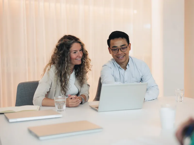 Two Axis colleagues sitting next to each other in a meeting room, looking jointly at a laptop screen.