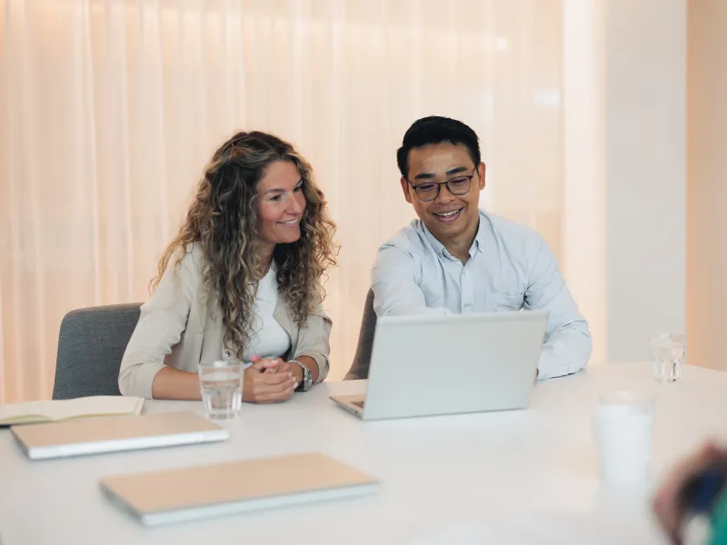 Axis colleagues sitting in a conference room, looking at a laptop screen together and smiling.