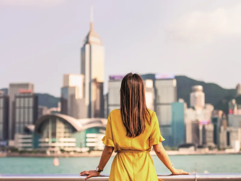 Woman in yellow dress looking over a bridge at a city.