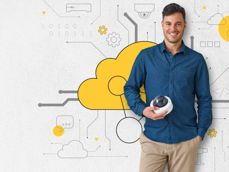 Man standing against a wall with cloud connect motive on it, holding an Axis camera.