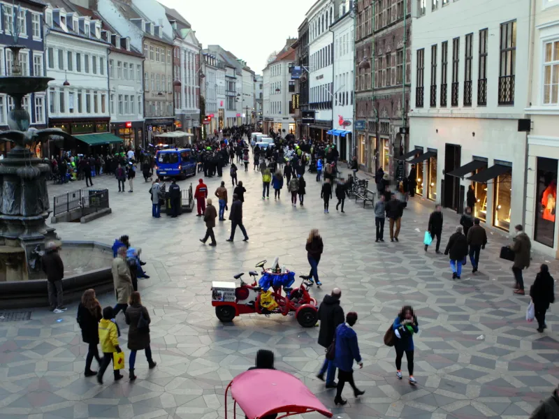 Town square in Copenhagen with people walking around. Shopping buildings are lined up both to the left and right.