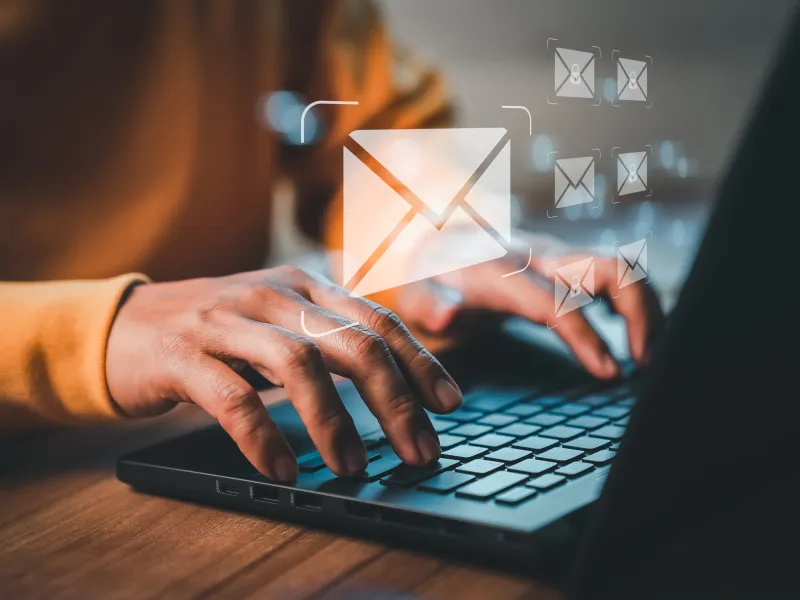 A person typing on a laptop. Visual e-mail symbols are floating above the hands.
