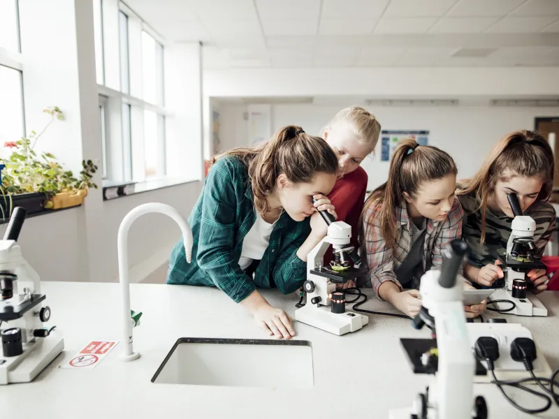Group of female students looking through a microscope in a school science lab.