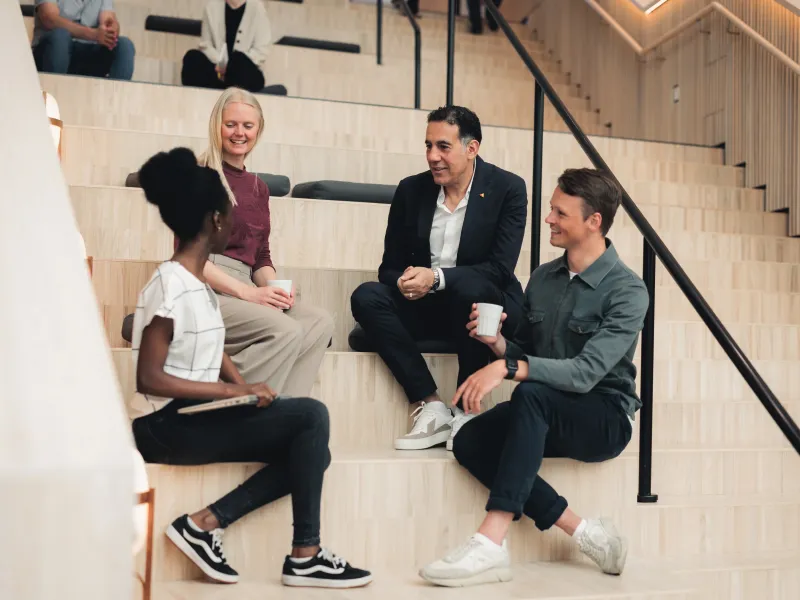 Axis colleagues sitting on the stairs at Grenden, Axis HQ in Lund, having a conversation and smiling.