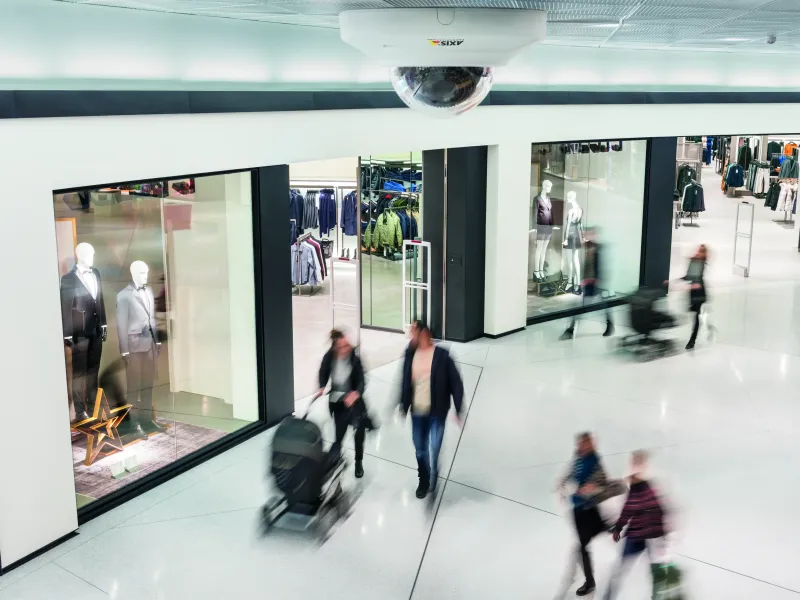 Axis network camera mounted on the roof of a shopping mall. People are walking outside the retail store.