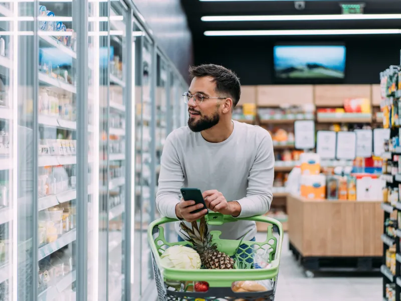A man with a shopping cart strolling down a grocery aisle.