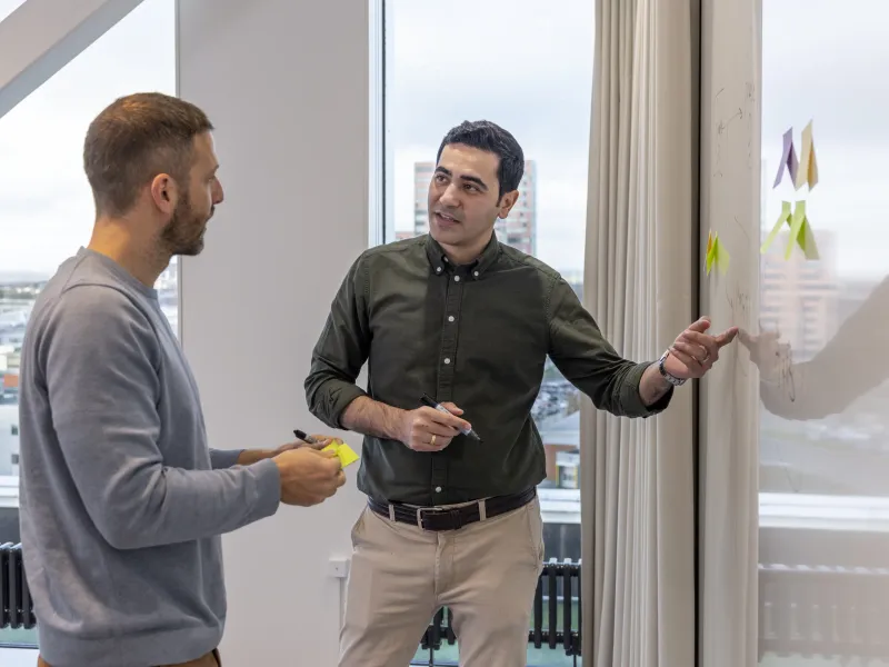 Axis colleagues standing in front of a whiteboard, collaborating and workshopping with post-it notes.