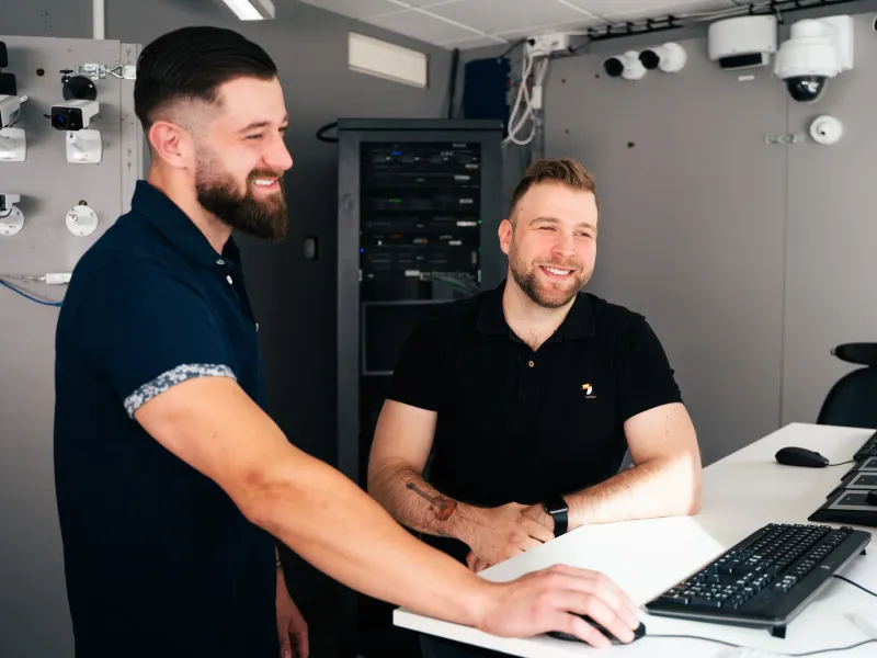 Two Axis colleagues standing by a desk, looking at the same screen and collaborating.