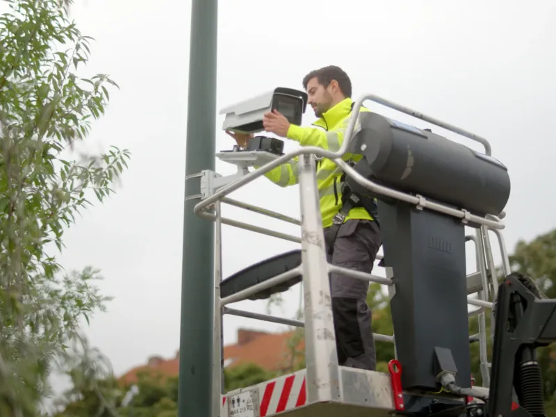 Box camera being installed on pole in front of trees