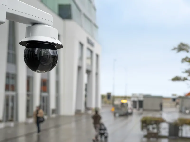 AXIS Q6325-LE PTZ Camera mounted in a city square. Big building to the left and open area to the right.