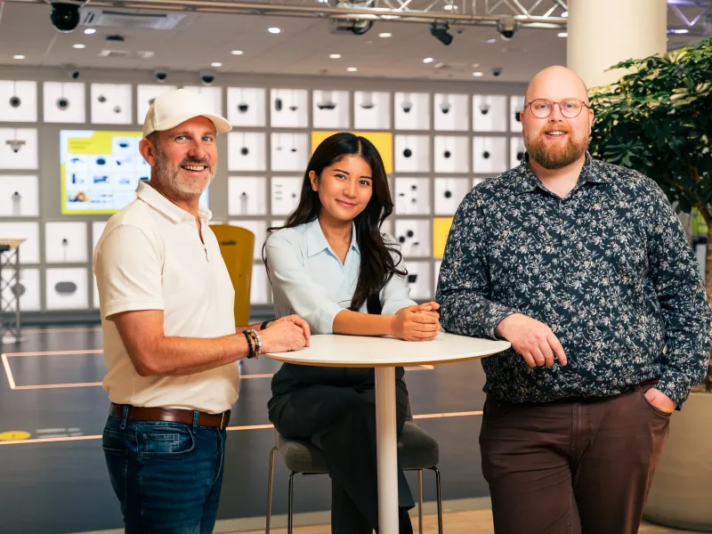 Three Axis employees in Lund AEC standing and sitting around a small round table.