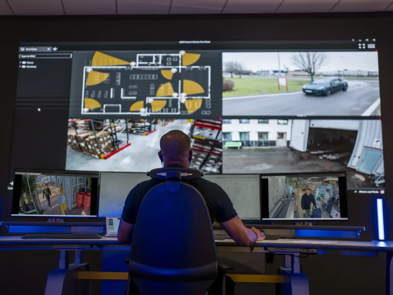 Security man looking over the area in a room with multiple screens.