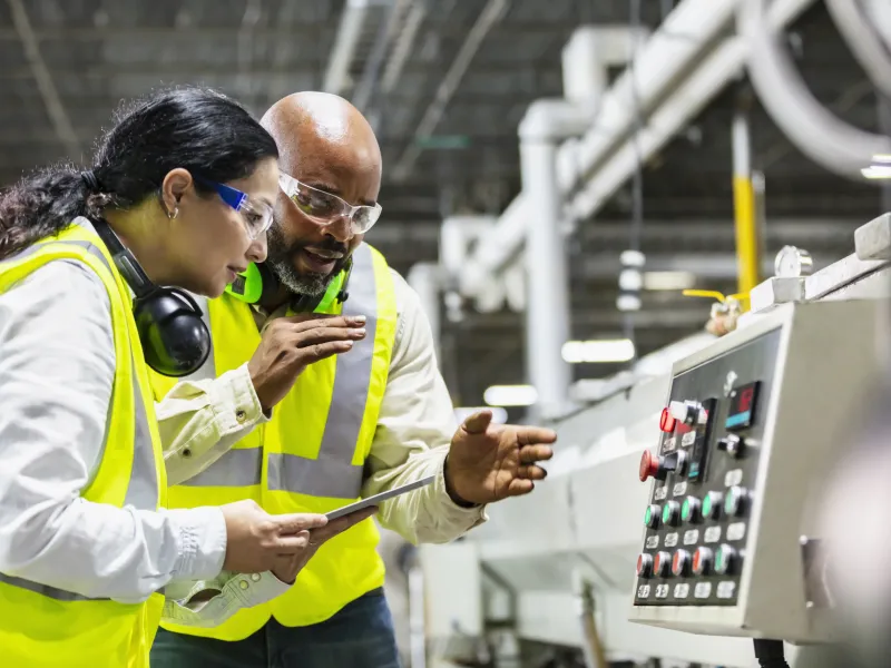 Two workers inspecting a machine control panel in a factory.