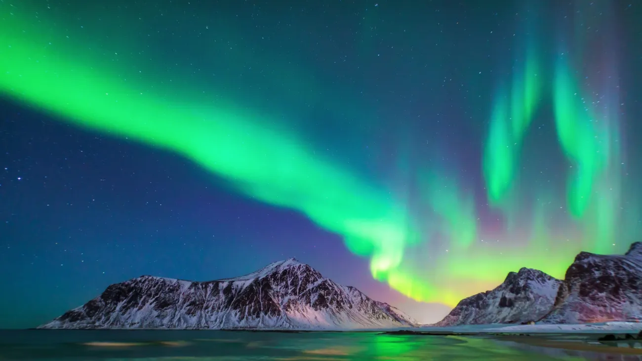 Mountain on the horizon of the sea with northern lights shining in the dark blue sky.