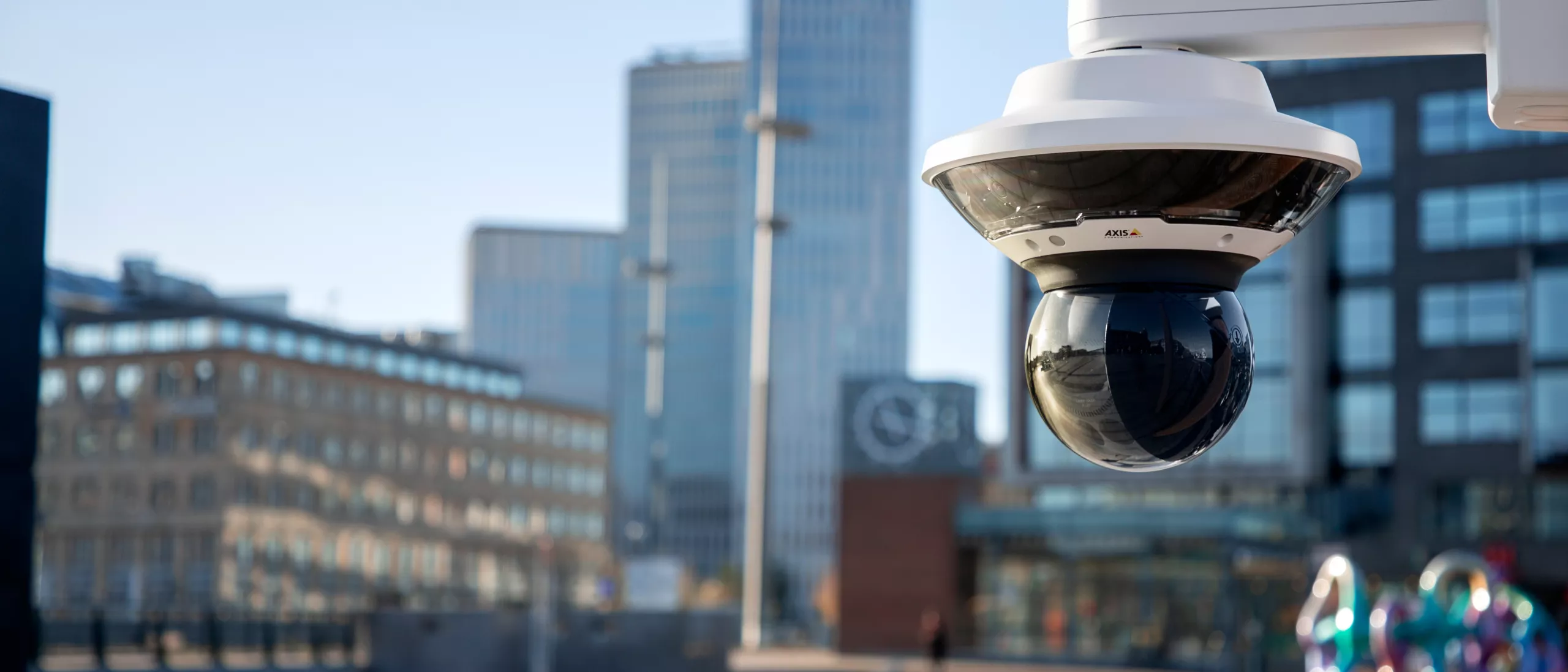 Axis dome camera surveilling over Malmo. Tall buildings in the background with a blue sky.