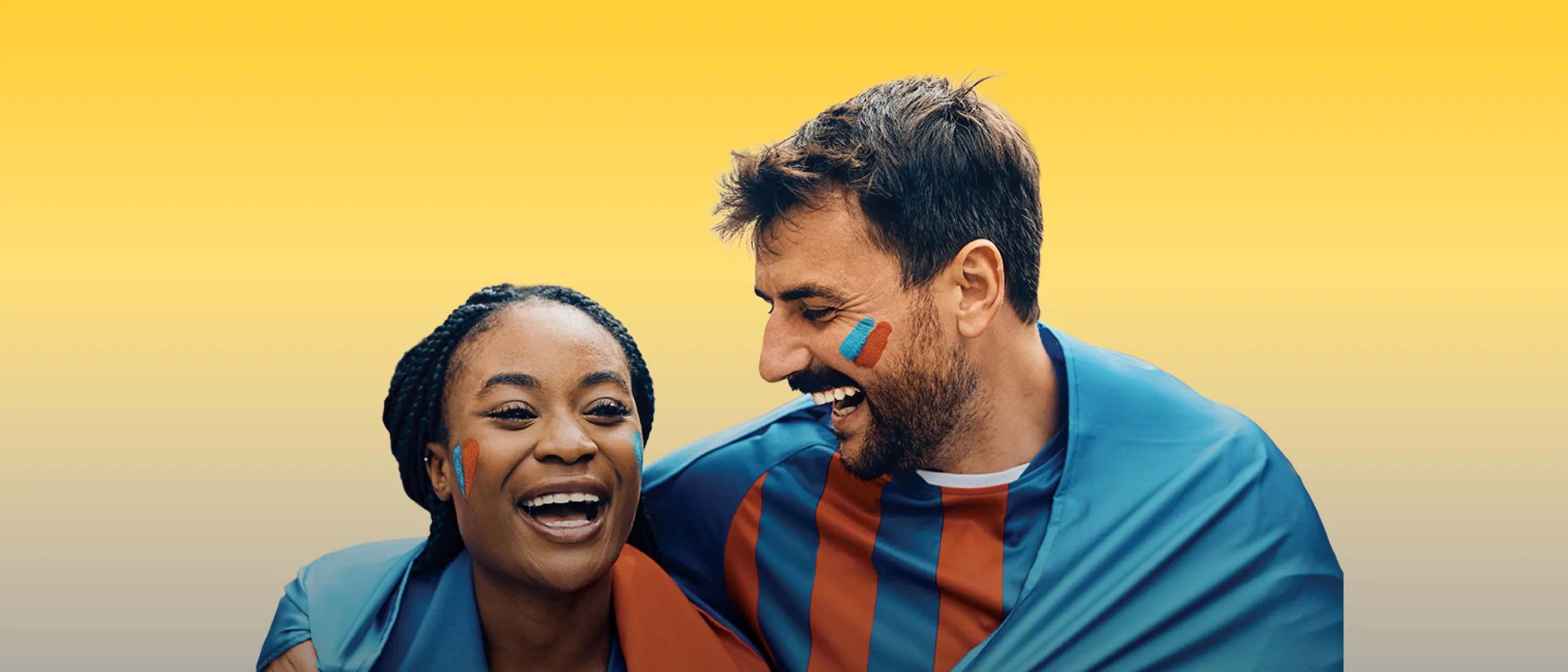 A woman and a man wearing soccer jerseys and happily holding on to each other in front of a yellow gradient background.