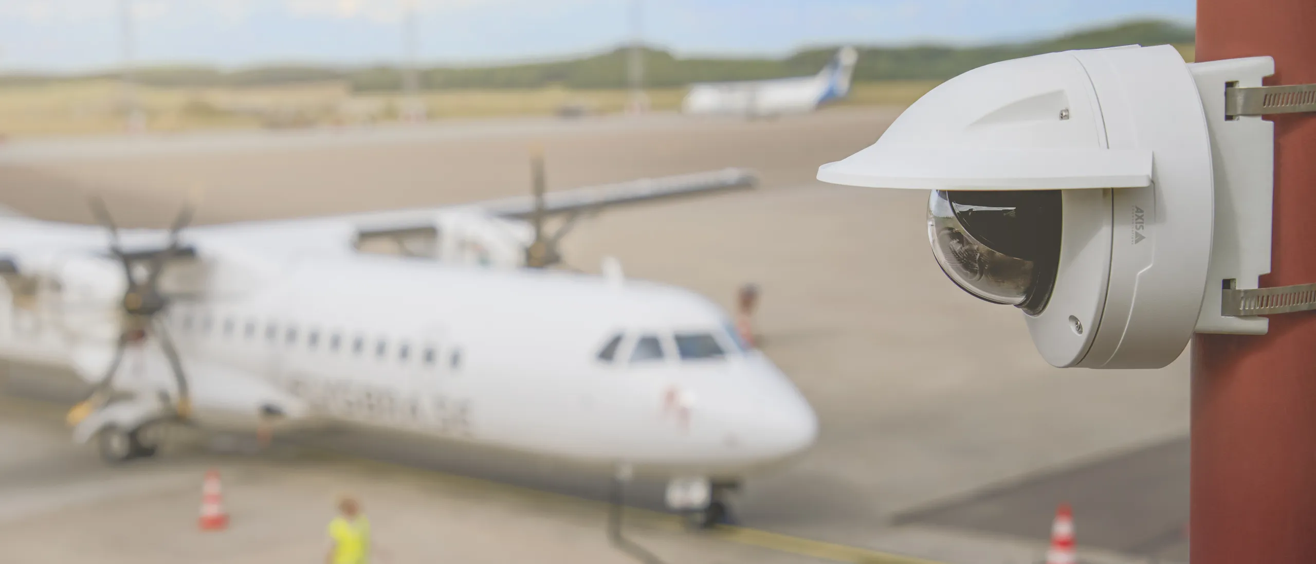 Axis network camera mounted on a wall outside an airport with an airplane in the background.