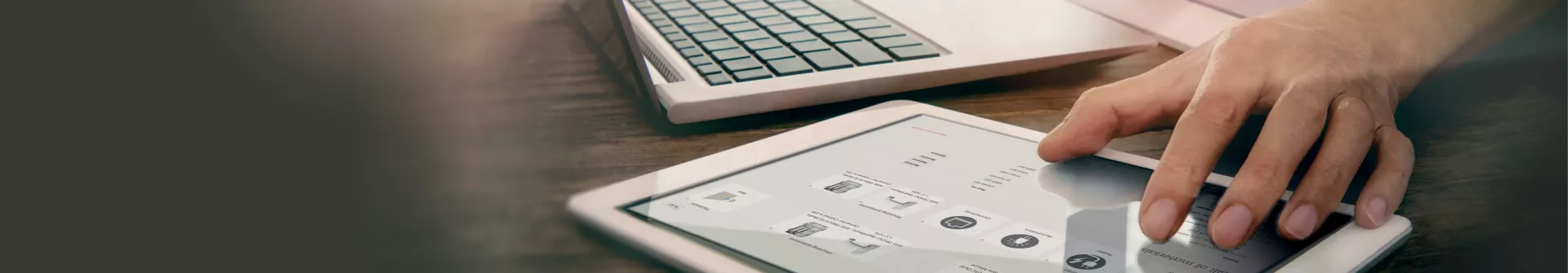 Hand on a tablet, with a laptop besides