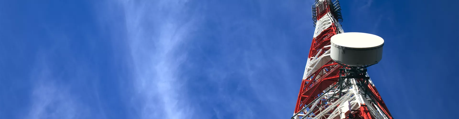 Red and white telecommunications tower in a blue sky