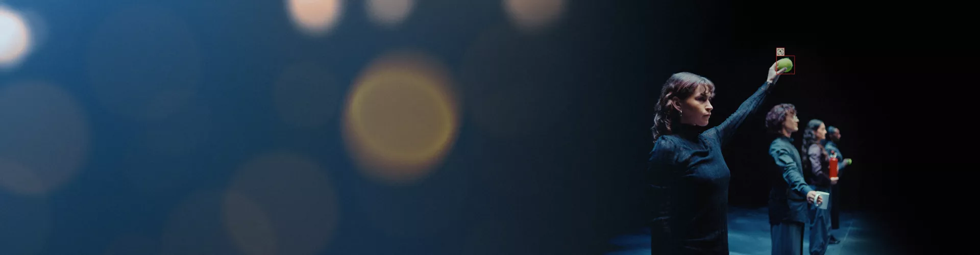 Four people are standing in a line. The first one, in the foreground, is holding a tennis ball.