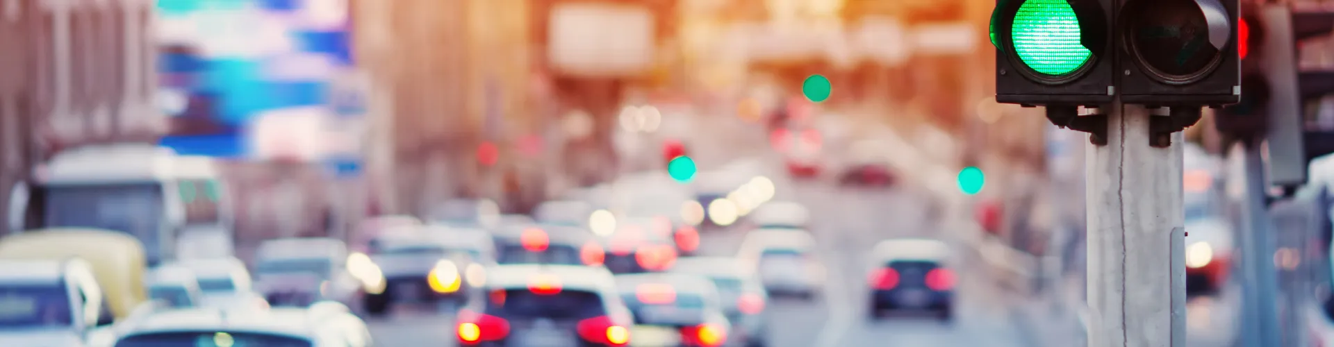 View of a blurry street with cars and a traffic light in focus showing the green light.