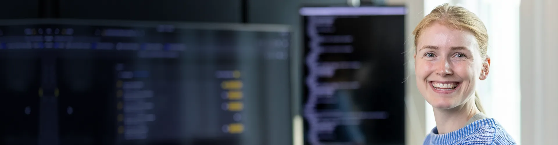 Amanda Håkansson, software engineer at Axis, smiling while monitoring two screens.