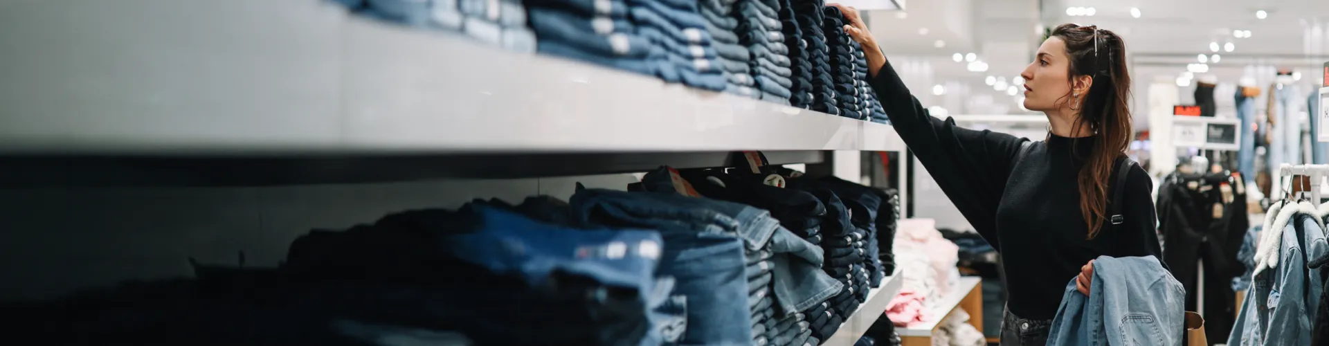 Young woman shopping for jeans in a retail store.