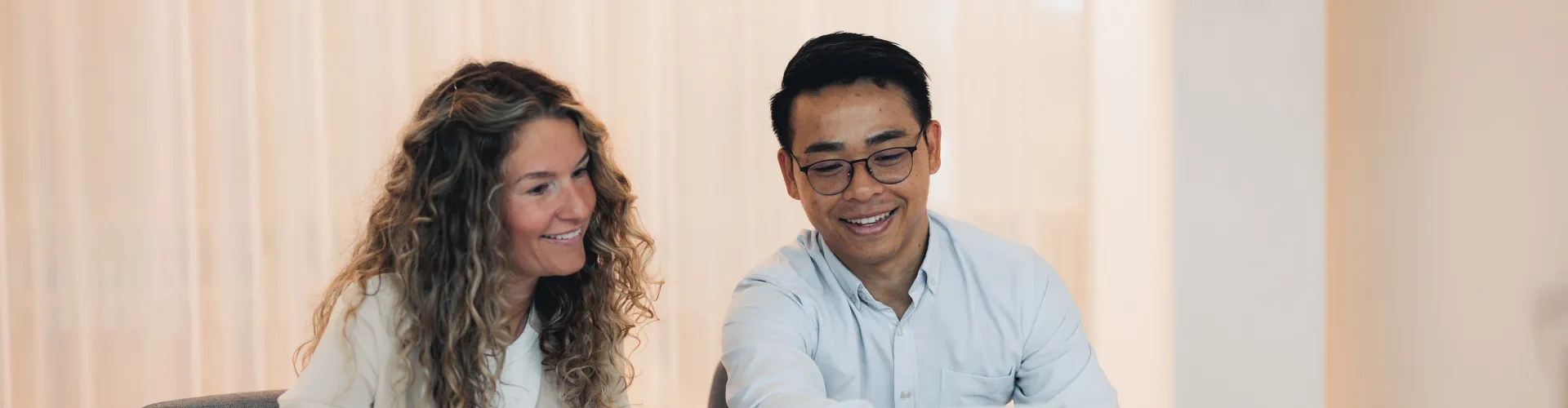 Anna Hall and James Chaiyasan happily looking at a laptop in a meeting room.
