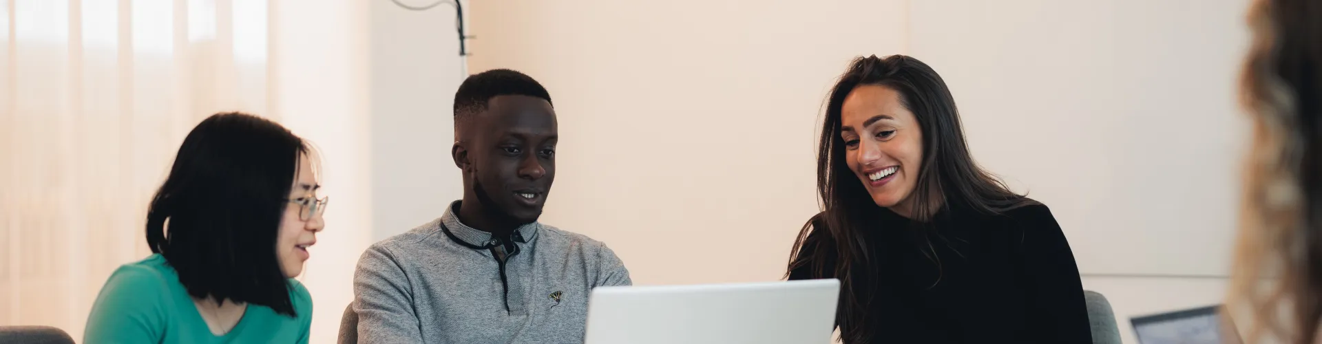 Three people sitting around a table and surrounding a laptop.