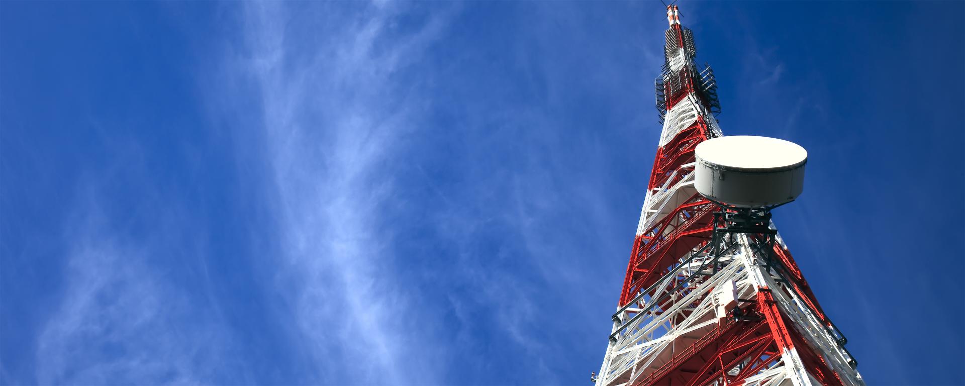 Red and white telecommunications tower in a blue sky