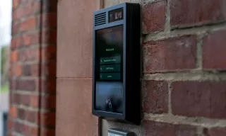 AXIS I8307-VE Network Video Intercom, mounted on a brick wall in an outdoor environment