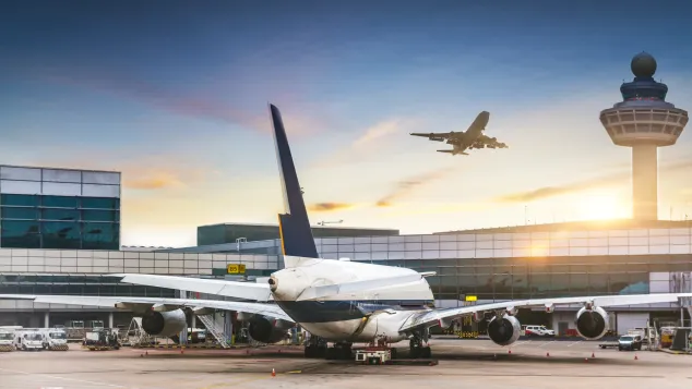 Airport during sunrise with one airplane stationed and another one taking off.