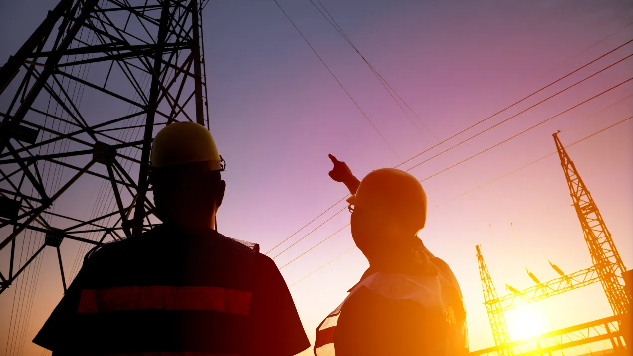 Two male engineers pinting at electrical pylon/transmission tower at sunglight