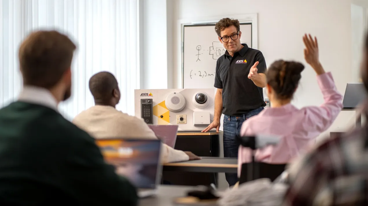 An Axis Academy trainer conducts a classroom training, demonstrating products to several participants.