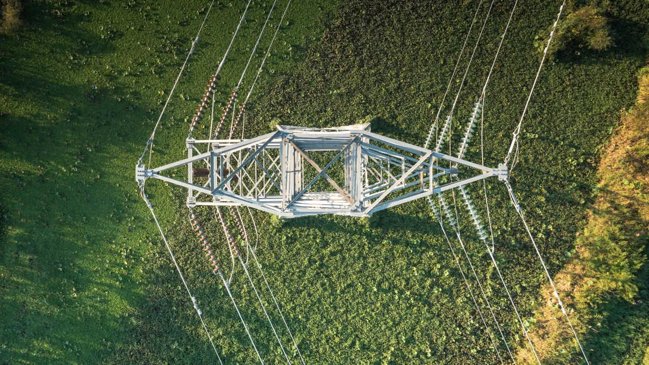 Electrical pylon transmission tower on a grass field from an aerial view.