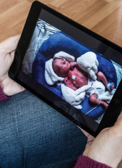 Female holding a tablet monitoring a newborn baby with tubes on body.
