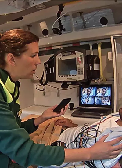 Two female paramedics in ambulance, one talking to male patient.