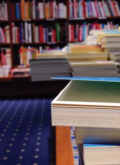 Stacked books with bookshelves in background